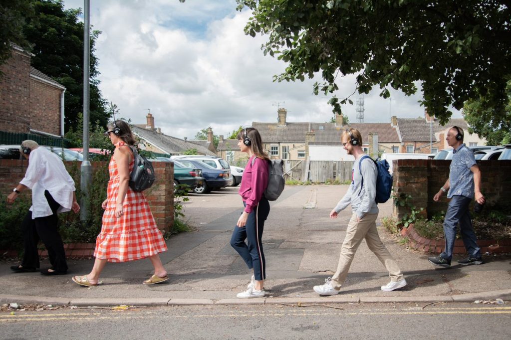 A photo of five people wearing headphones and walking along a street.