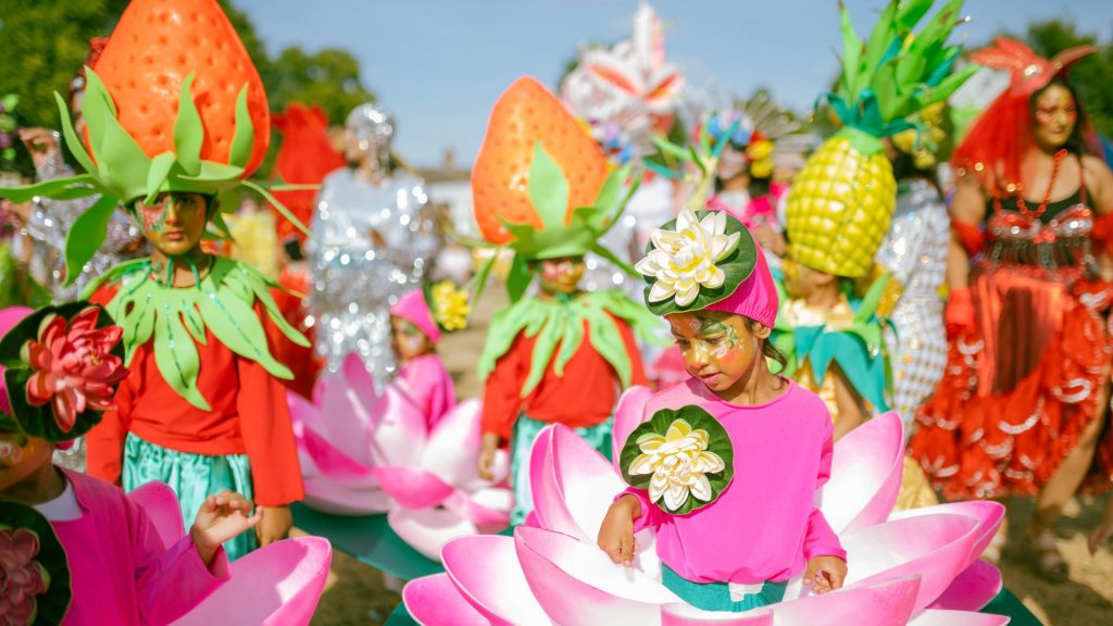 A photo of children and adults dressed in vibrant carnival costumes. Strawberry, lotus and pineapple costumes.