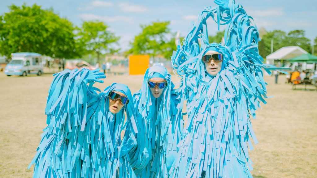 a photo of three strange blue creatures posing on the grass at Millfield Festival