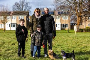 A family with two children pose with their two small dogs. Stood on the grass with houses in the background. The event was WestWoof dog walk and social in Westwood, Peterborough.