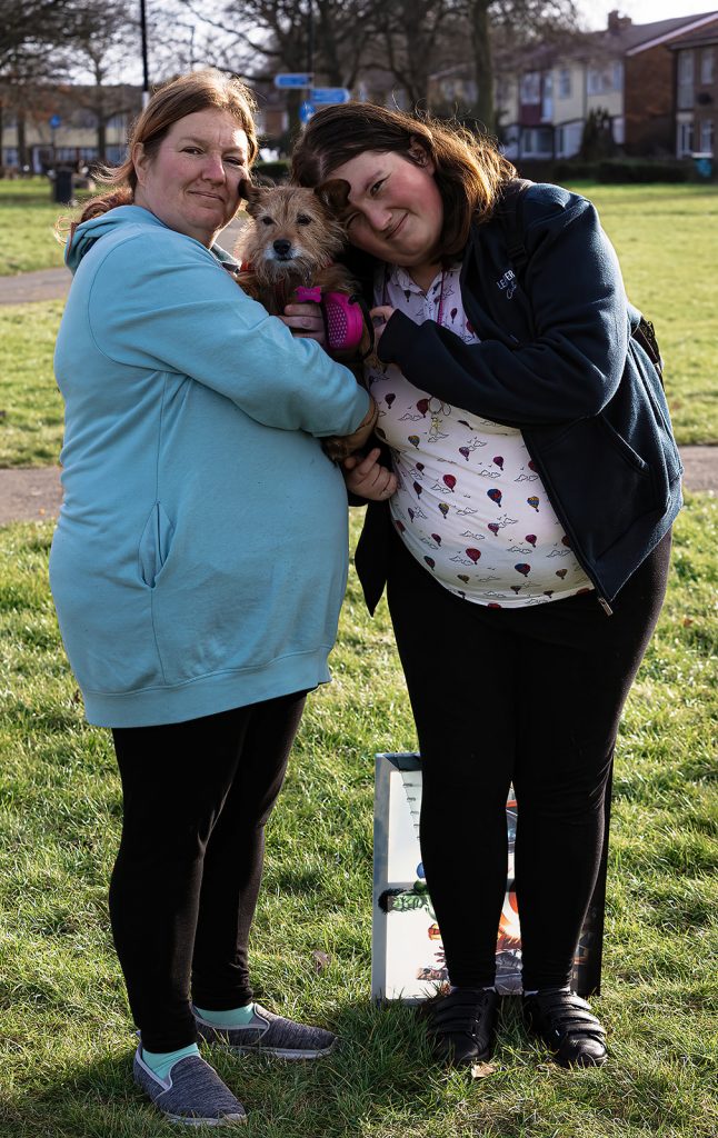 A mum and her daughter pose with their small terrier dog. Stood on the grass. The event was WestWoof dog walk and social in Westwood, Peterborough.
