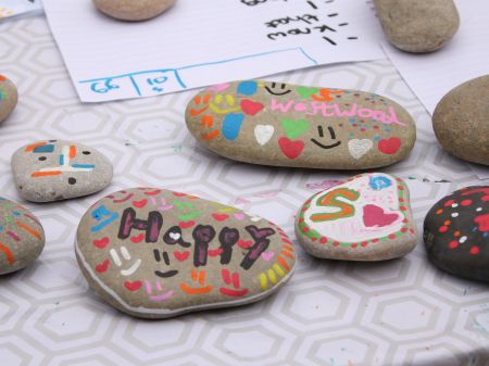 An assortment of large pebbles that have been decorated with words and doodles. The word "happy" is written on one pebble and the word "westwood" is written on another