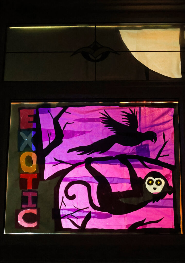 Exotic pet refuge decorated window. Saying Exotic down the left hand side and various animals - a bird, a monkey silhouetted in the main image. A purpley background.