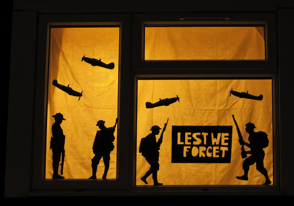 A black and white decorated window. A 'Lest We Forget' on a sign with silhouettes of soldiers and planes.