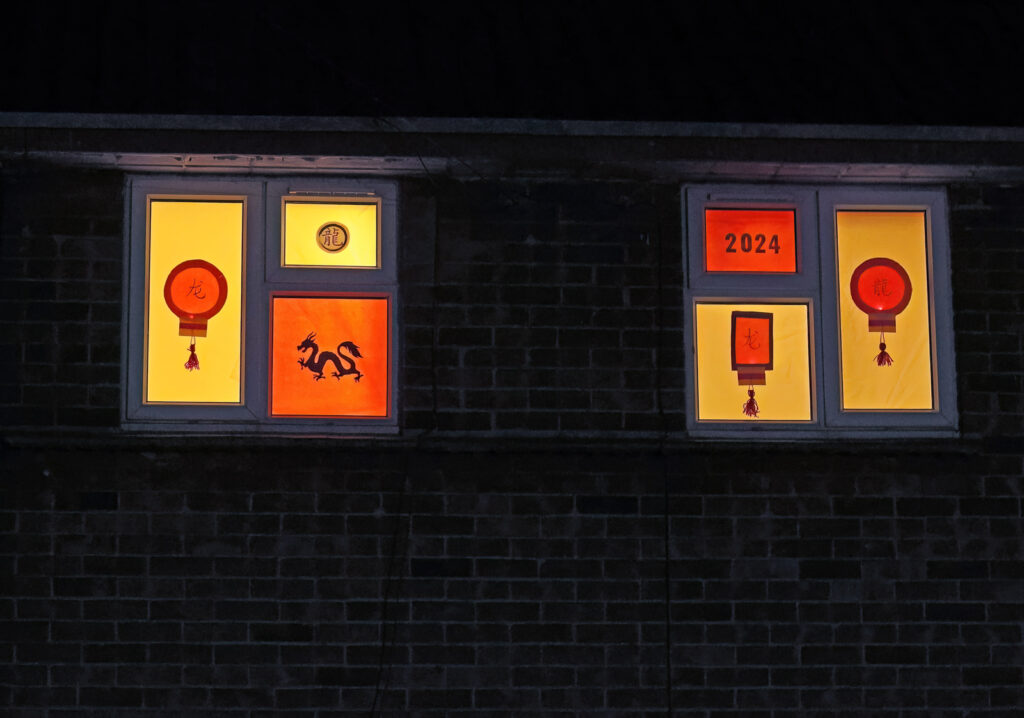 A window design over 2 sets of windows. Yellow and orange colours of lanterns and a dragon.