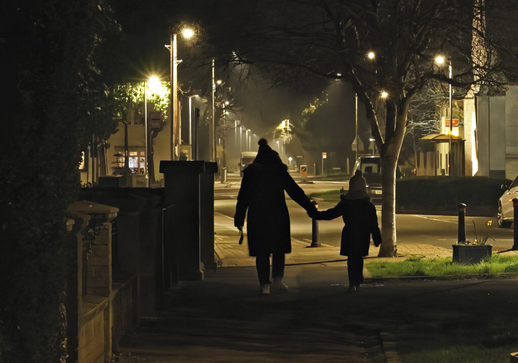 A calm village scene at Eye Villahe. an adult and child walking hand in hand down the evening lit street
