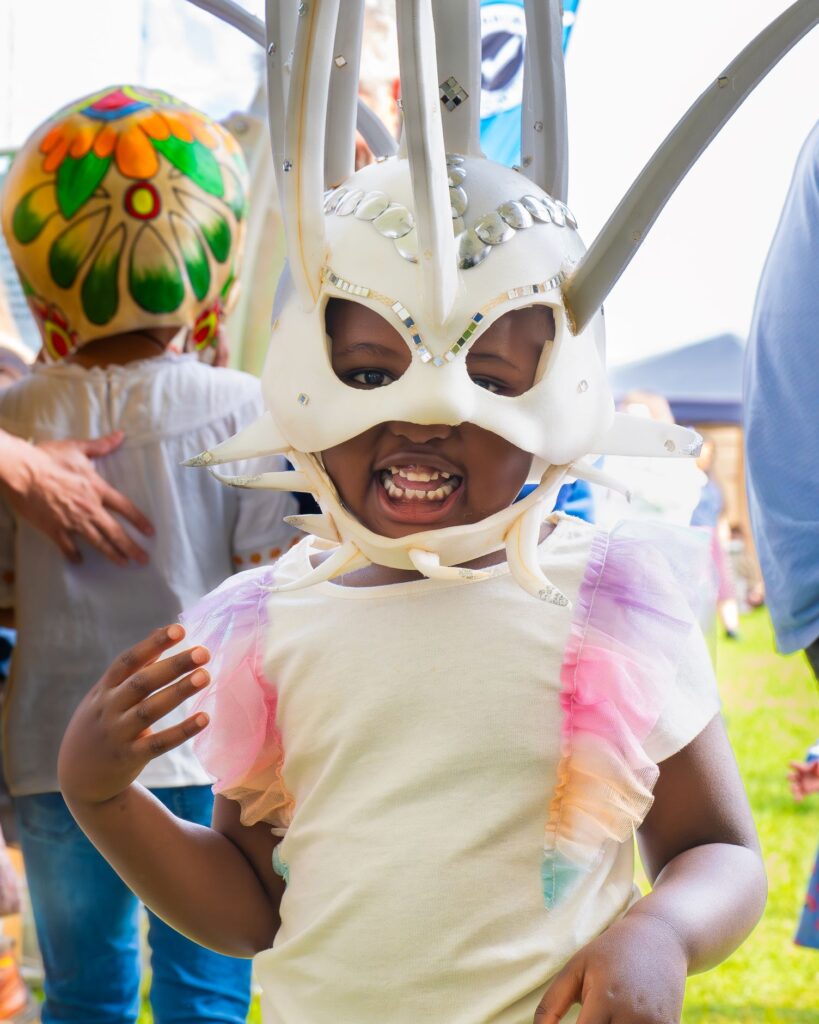 In the Creative dome at the Peterborough Celebrated Festival.... A young girl with a pale and colourful summer top on, is facing the camera and has a large white carnival hat on.