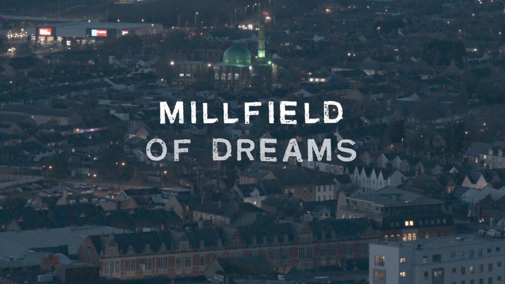 A screenshot from the opening title of Millfield of dreams. The image is drone footage in the evening of the Millfield residential area. The green mosque minarets are beautifully illuminated