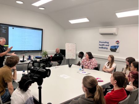 Young people sat around a table in a clean white classroom, looking at Stu from Lemonwedge who is talking at the group. There is some film-related information on the large screen behind Stu.