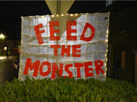 A paper sign reading "Feed the monster" written in red type against the white background. It is leant up against a sign and has lights framing the outside of the design.
