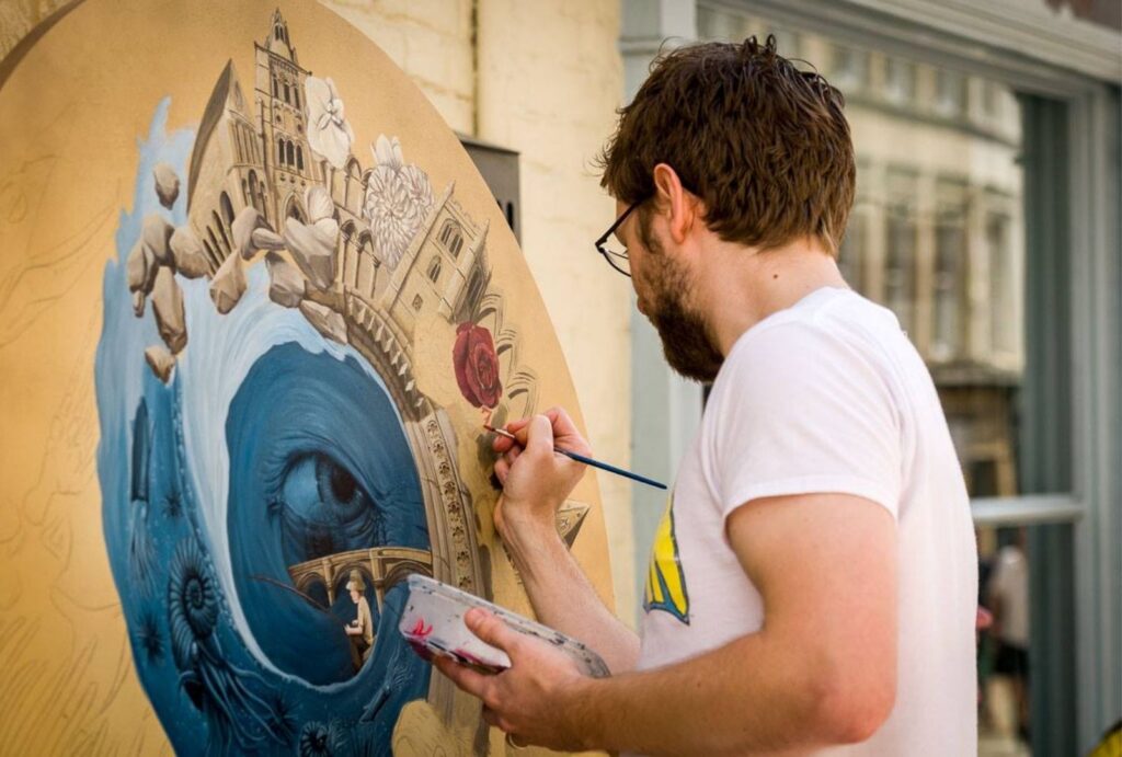 An image of local artist Jason Duckmanton. In the image his back is turned and he is hand painting onto a canvas.