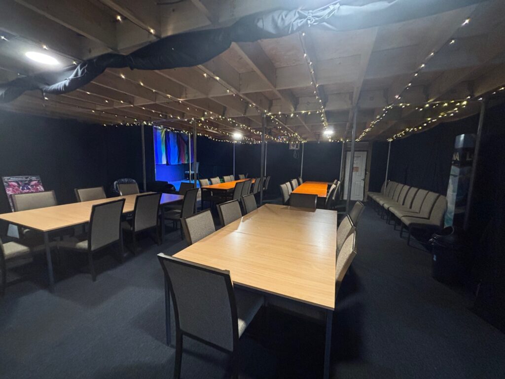 a photo of the classroom in angle gaming lounge. A darkly lit gaming lounge with large tables and chairs