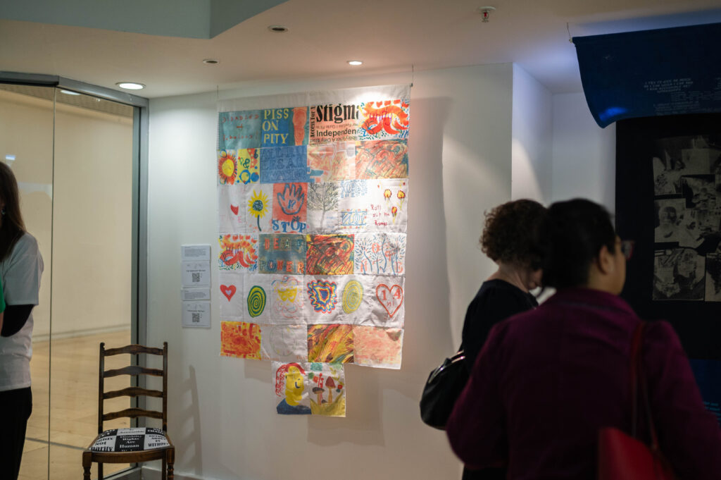 The Power of Protest and Print exhibition. A patchwork fabric artwork made up of colourful, hand-printed rectangles. Each patch was made by a DDN person in a workshop with Fae.