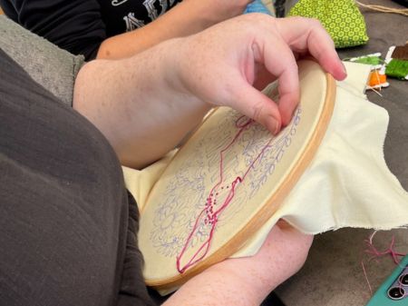 A close up of a person sewing at a stitch and bitch session