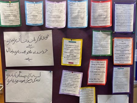 A notice board display of children's poetry. Most have been printed with a colourful border around them. On the left, two a3 sheets of urdu script are also pinned to the board.