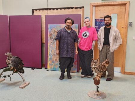 seyyed, charley, and zain stood posing behind two birds of prey, an eagle on the left and an owl on the right.