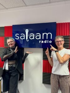 Charley and Sarah pose in front of the salaam radio logo in their studio.