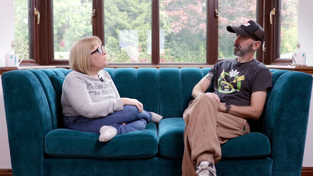 Julie Fernandez (left) in conversation with Jay Gearing (right). They are sat on a sapphire blue sofa.