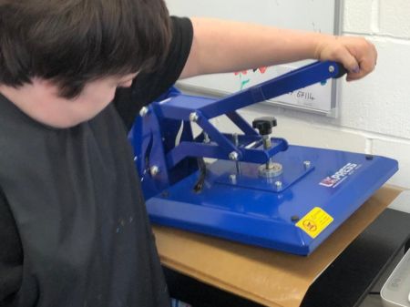 A person using a blue heat press. Their hand holds the lever, pushing the press down.