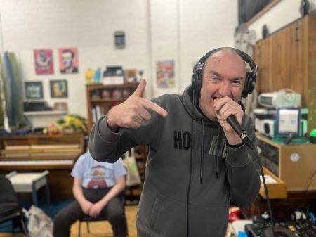 A DDN person holding a mic and wearing headphones, posing playfully with one finger pointed to the camera, in a typical hip hop pose.