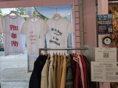 Three white protest t-shirts on display in the window of Sue Ryder charity shop.