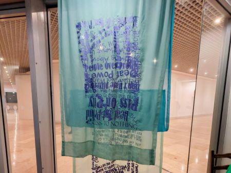 A thin chiffon fabric panel artwork hangs in a folded, layered way in the window of the exhibition space.