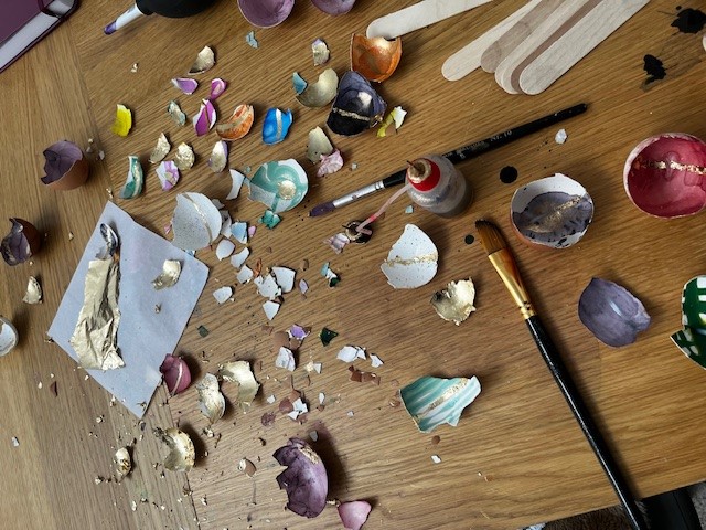 an overhead shot of the kintsugi eggshell painting activity. Lots of metallic coloured eggshell segments are scattered on the table amongst paints and brushes.