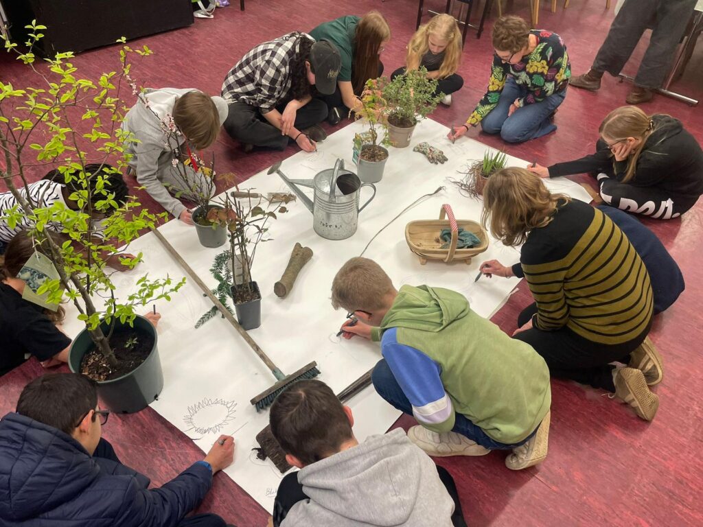 7 of Eye Village's young people working together on a collective piece on the floor. With sprigs of nature around them too.