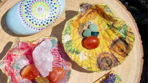A close up of a colourfully decorated rock, and 2 decorated / decoupage shells, holding a crystal.