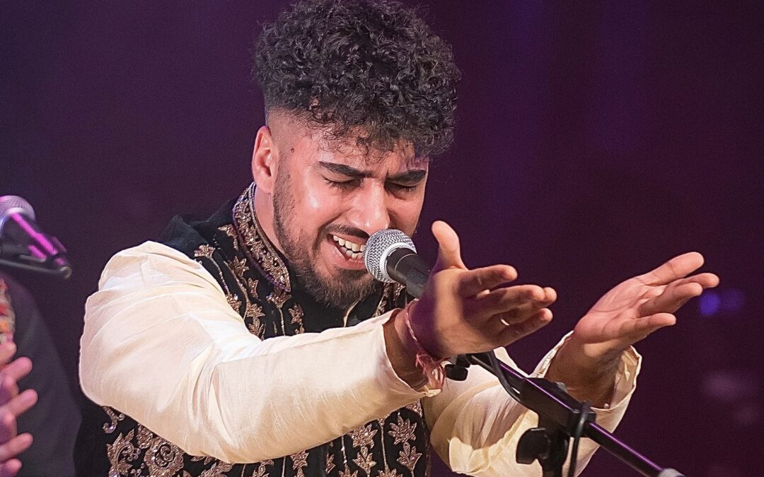 chand ali khan singing into the microphone. His eyes are closed and his hands are outstretched, palms upwards. He is wearing traditional shalwar kameez.
